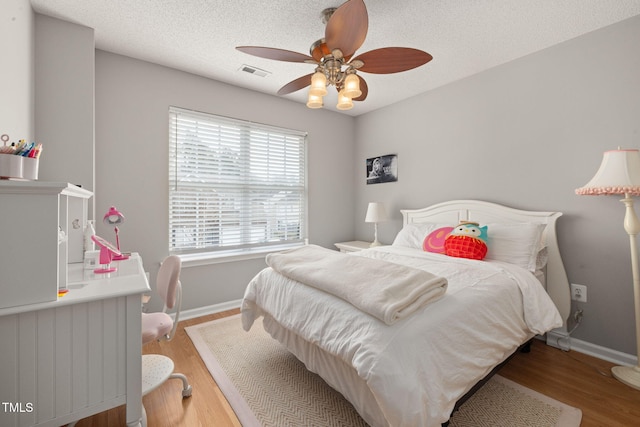 bedroom with visible vents, ceiling fan, baseboards, wood finished floors, and a textured ceiling