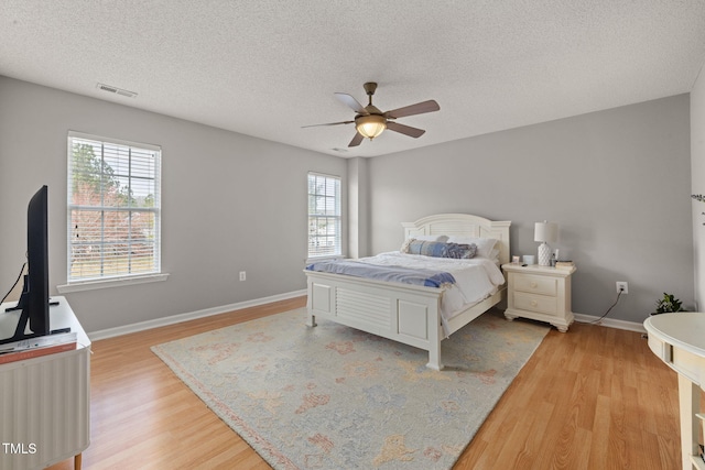 bedroom with a ceiling fan, baseboards, visible vents, a textured ceiling, and light wood-type flooring