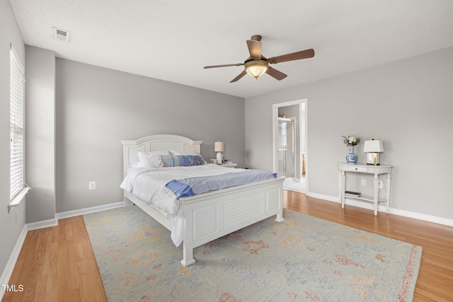 bedroom featuring a ceiling fan, baseboards, visible vents, light wood finished floors, and a textured ceiling