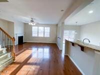 unfurnished living room with wood finished floors, a fireplace, baseboards, ceiling fan, and stairs