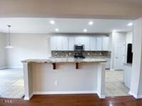 kitchen with stainless steel microwave, pendant lighting, recessed lighting, a kitchen breakfast bar, and wood finished floors