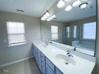 full bathroom with double vanity, baseboards, and a shower stall