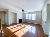 unfurnished living room with a fireplace, wood finished floors, baseboards, and ceiling fan