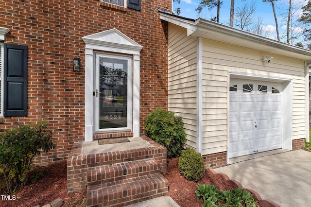 doorway to property with concrete driveway, an attached garage, and brick siding