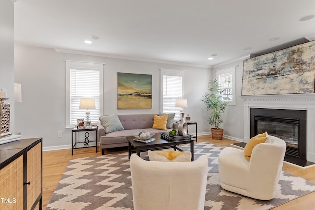 living room featuring a glass covered fireplace, crown molding, light wood-type flooring, and baseboards