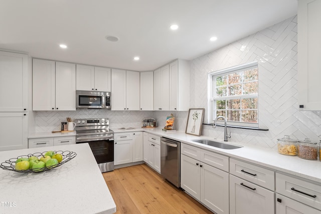 kitchen with white cabinets, appliances with stainless steel finishes, light wood-style flooring, and a sink