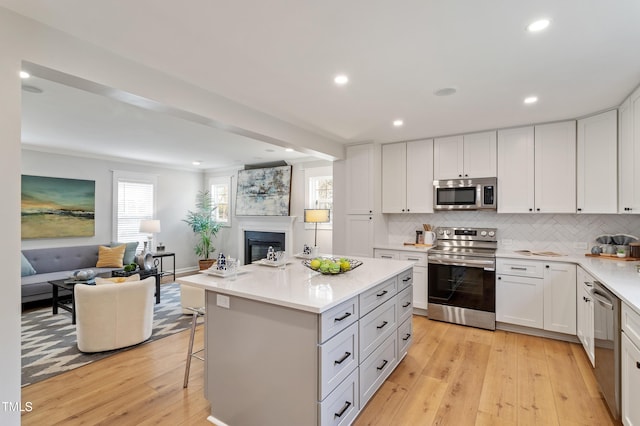 kitchen featuring a kitchen breakfast bar, open floor plan, stainless steel appliances, light wood-style floors, and light countertops