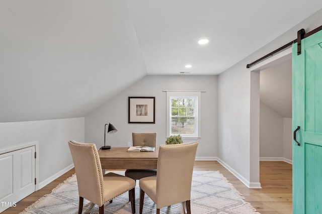 dining space with lofted ceiling, baseboards, light wood-type flooring, and a barn door