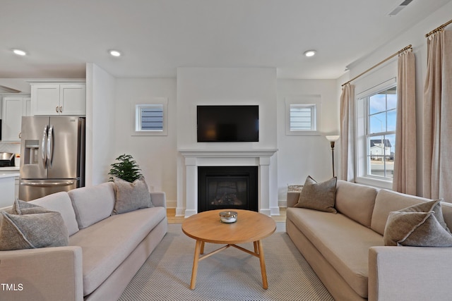 living area featuring recessed lighting, visible vents, baseboards, and a glass covered fireplace