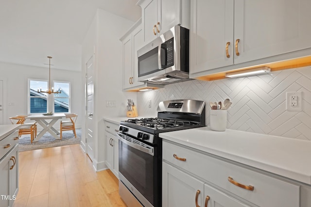 kitchen with a notable chandelier, appliances with stainless steel finishes, light wood finished floors, decorative backsplash, and light countertops