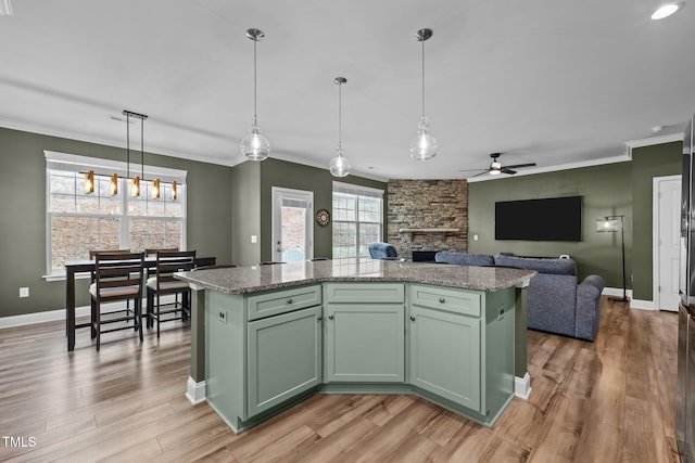 kitchen featuring green cabinets, ornamental molding, a stone fireplace, light wood-style floors, and hanging light fixtures