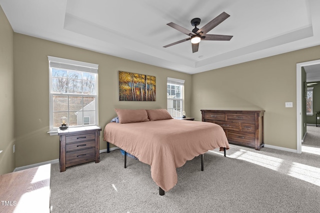 carpeted bedroom featuring baseboards, a tray ceiling, and a ceiling fan