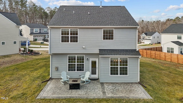 rear view of property with a fire pit, fence, roof with shingles, a yard, and a patio area