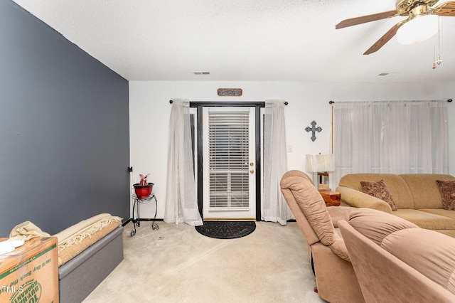 living area with visible vents, light colored carpet, a textured ceiling, and ceiling fan