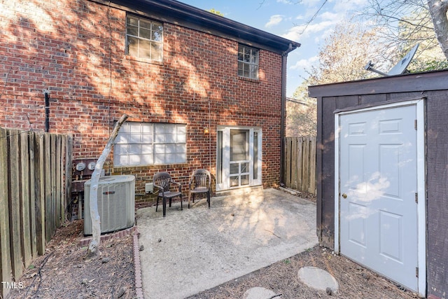 back of property with a patio, a fenced backyard, an outdoor structure, central air condition unit, and brick siding