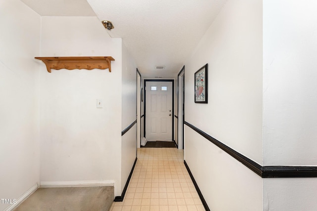 hall featuring visible vents, baseboards, and a textured ceiling