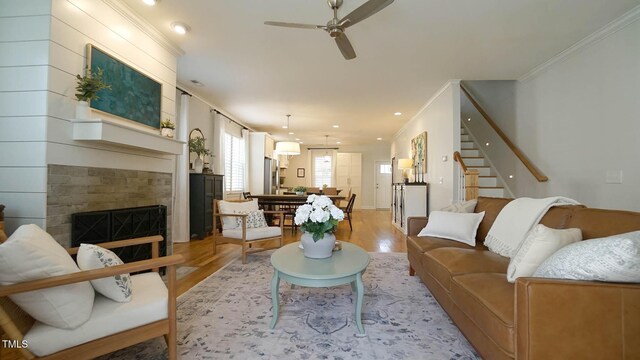 living area with stairway, a fireplace, light wood-style flooring, and crown molding