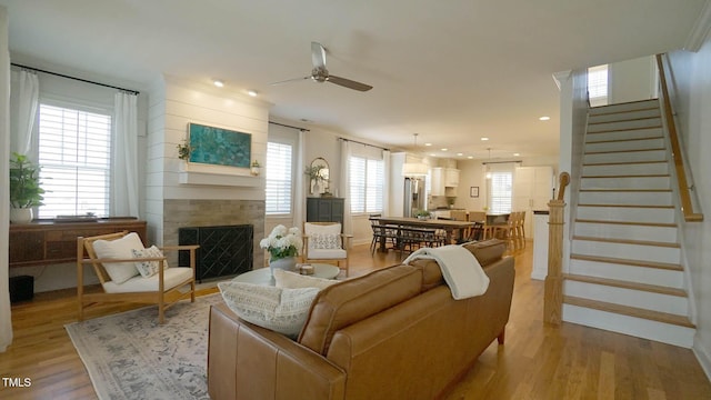 living area with a ceiling fan, a tiled fireplace, recessed lighting, light wood finished floors, and stairs