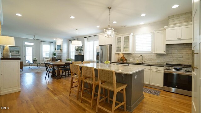 kitchen featuring light wood-style flooring, a sink, a center island, stainless steel appliances, and decorative backsplash