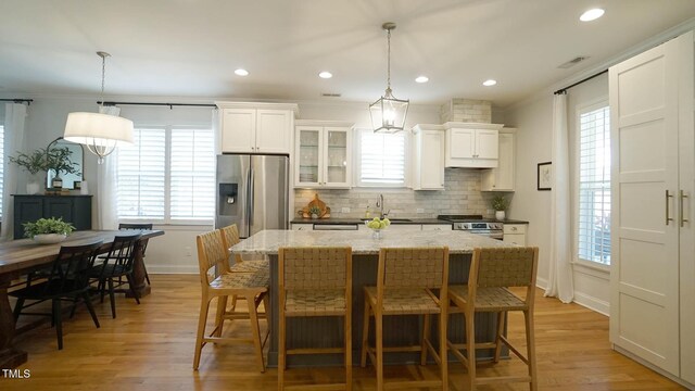 kitchen with light wood-style flooring, a kitchen island, tasteful backsplash, appliances with stainless steel finishes, and white cabinets