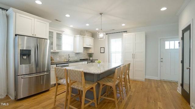 kitchen with white cabinetry, stainless steel appliances, light wood-type flooring, and ornamental molding