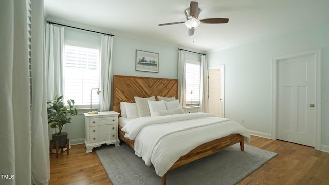 bedroom featuring a ceiling fan, multiple windows, baseboards, and light wood-type flooring