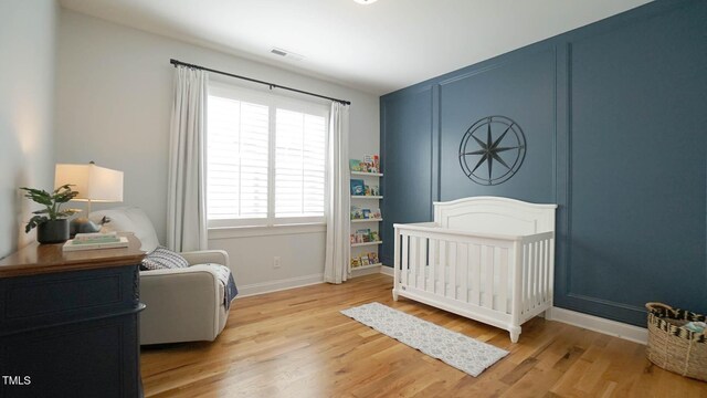 bedroom with a nursery area, light wood-style floors, visible vents, and baseboards