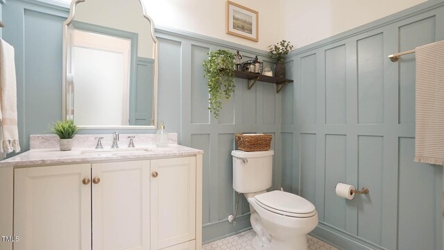 bathroom with vanity, a decorative wall, and toilet