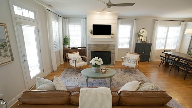 living room featuring light wood-style flooring, a fireplace, a ceiling fan, and a healthy amount of sunlight