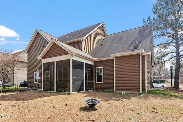 back of property with a fire pit, a trampoline, and a sunroom