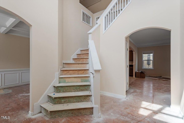 staircase with a decorative wall, wainscoting, arched walkways, and ornamental molding