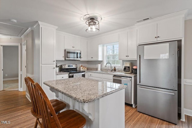 kitchen featuring a kitchen bar, visible vents, a sink, stainless steel appliances, and white cabinets