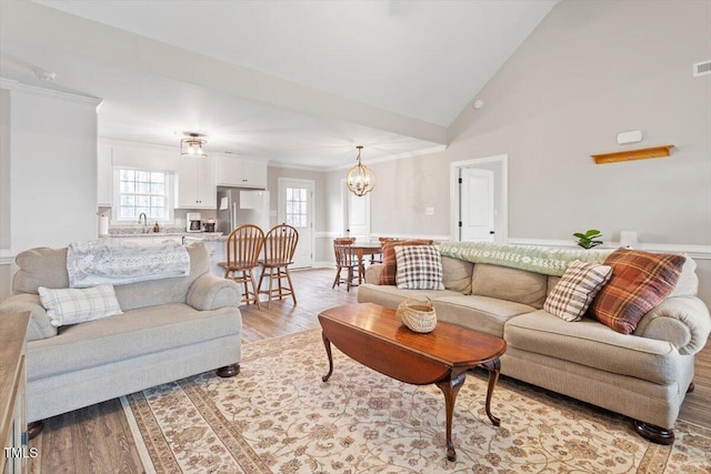 living area with visible vents, a chandelier, ornamental molding, light wood-style flooring, and high vaulted ceiling