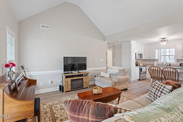 living room with light wood-type flooring, visible vents, baseboards, and high vaulted ceiling