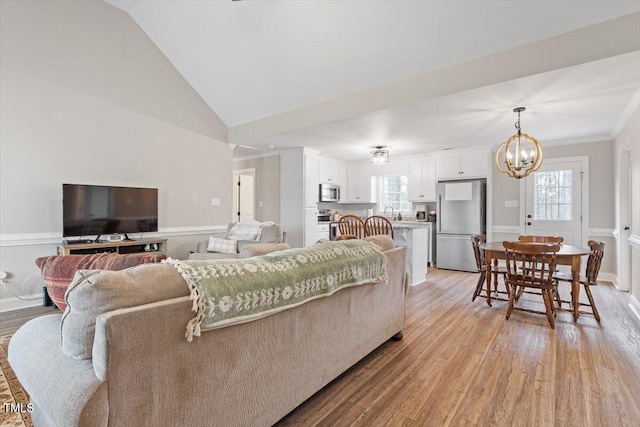 living room featuring vaulted ceiling, crown molding, light wood-style floors, and a chandelier