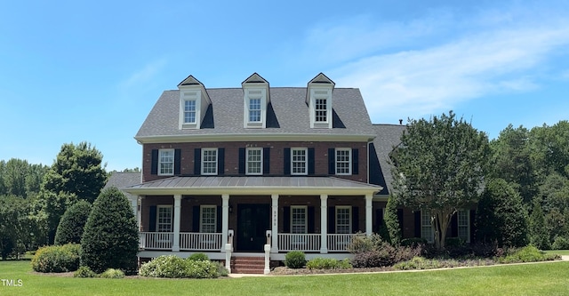 view of front of home with a front lawn, brick siding, covered porch, and roof with shingles