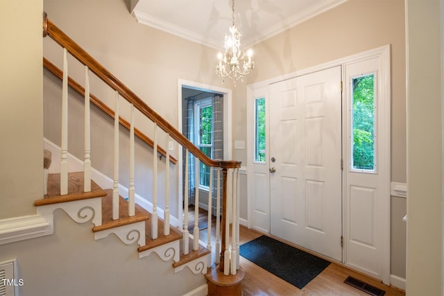 foyer entrance featuring visible vents, wood finished floors, crown molding, a chandelier, and stairs