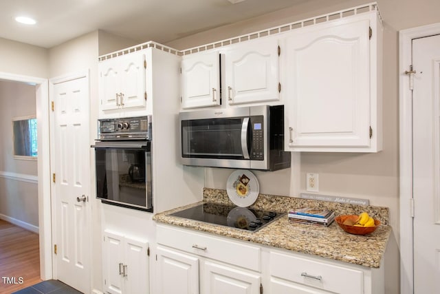 kitchen with light stone counters, black appliances, recessed lighting, and white cabinetry