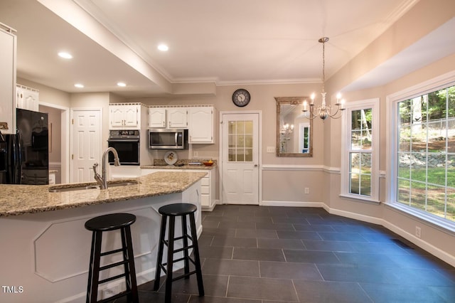 kitchen with light stone countertops, ornamental molding, a sink, black appliances, and white cabinetry