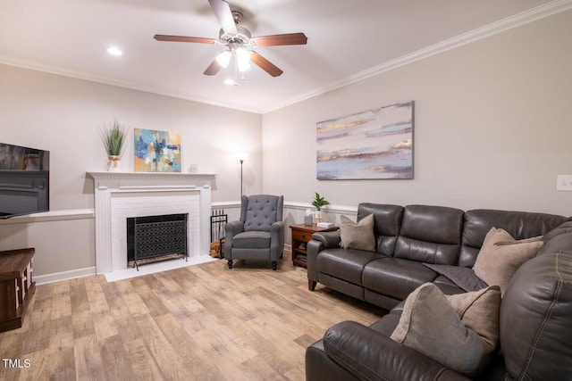 living area with baseboards, ceiling fan, a fireplace with flush hearth, ornamental molding, and light wood-style flooring