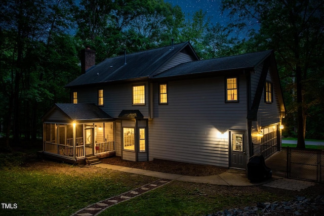 back of property featuring a gate, fence, a yard, a sunroom, and a chimney