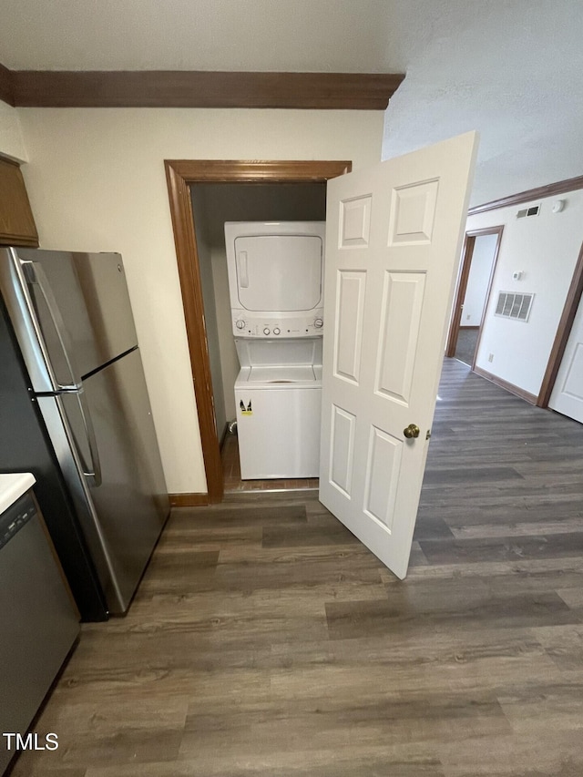 hallway featuring dark wood finished floors, stacked washer / dryer, baseboards, and visible vents