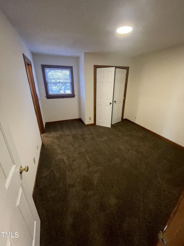 unfurnished bedroom with a closet, baseboards, and dark carpet