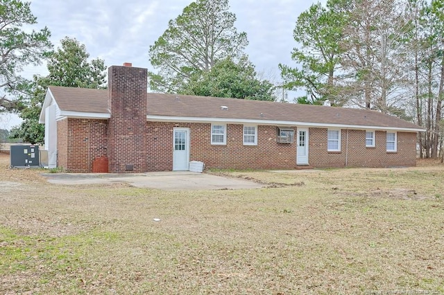 back of house with a patio, a lawn, brick siding, and a chimney