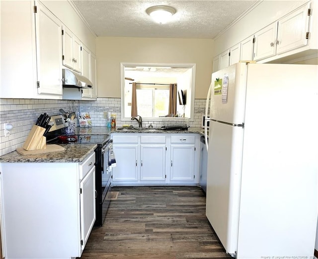 kitchen featuring under cabinet range hood, dark stone countertops, white cabinetry, freestanding refrigerator, and stainless steel electric range oven