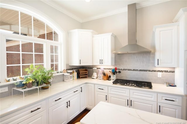 kitchen with tasteful backsplash, wall chimney range hood, ornamental molding, stainless steel gas stovetop, and white cabinetry