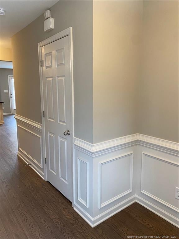 corridor featuring dark wood finished floors, a decorative wall, and a wainscoted wall