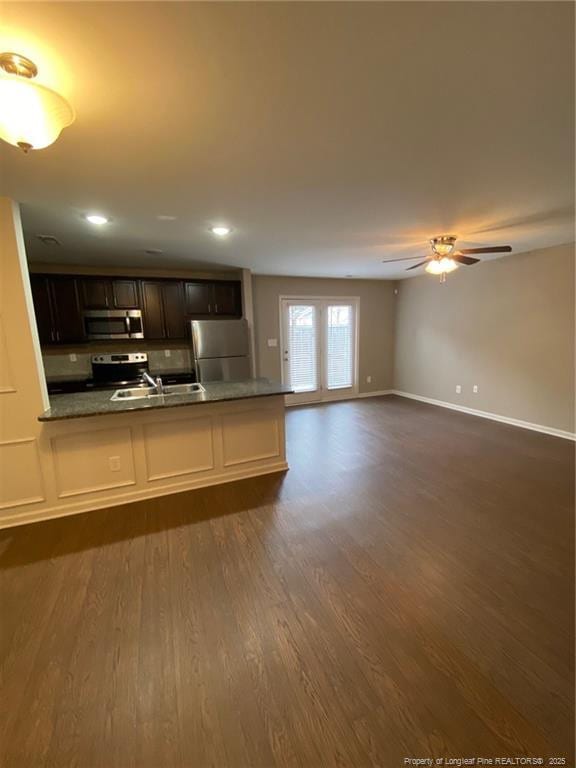 kitchen with a sink, baseboards, appliances with stainless steel finishes, and dark wood-style floors