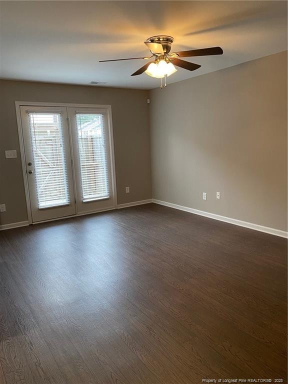 empty room featuring dark wood finished floors, a ceiling fan, and baseboards