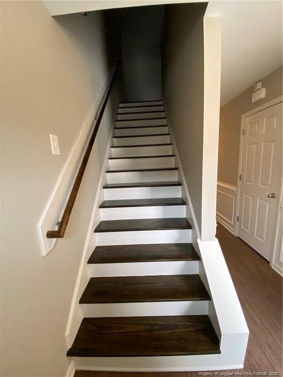 stairway with a wainscoted wall and wood finished floors